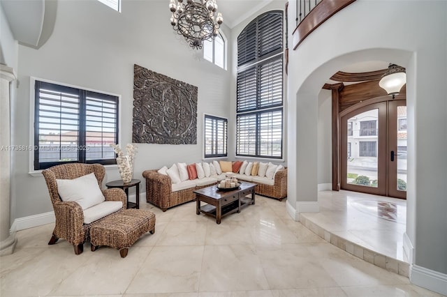 living room with french doors, a towering ceiling, crown molding, and an inviting chandelier