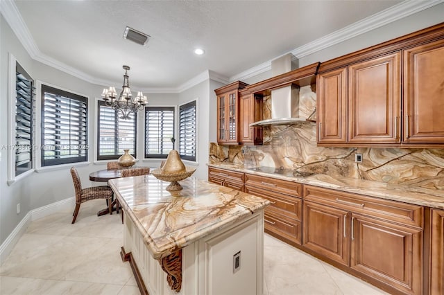 kitchen with wall chimney range hood, backsplash, light stone counters, a notable chandelier, and a kitchen island