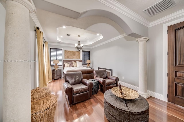 bedroom with an inviting chandelier, wood-type flooring, ornamental molding, a tray ceiling, and decorative columns