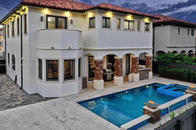 back house at dusk featuring a swimming pool with hot tub and a patio area