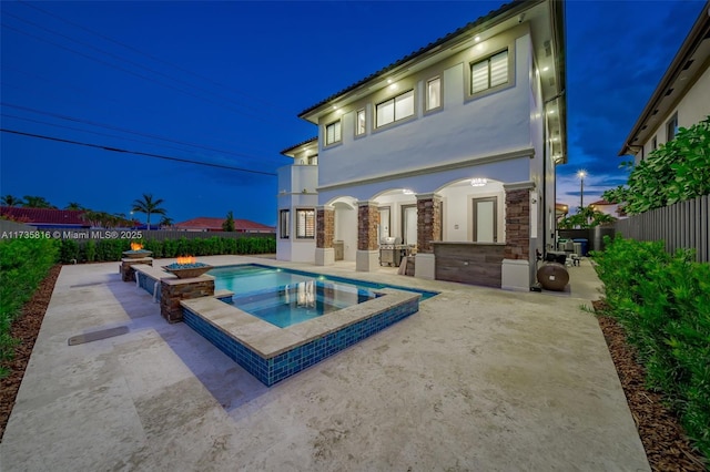 back of property with a fire pit, a patio area, and an in ground hot tub