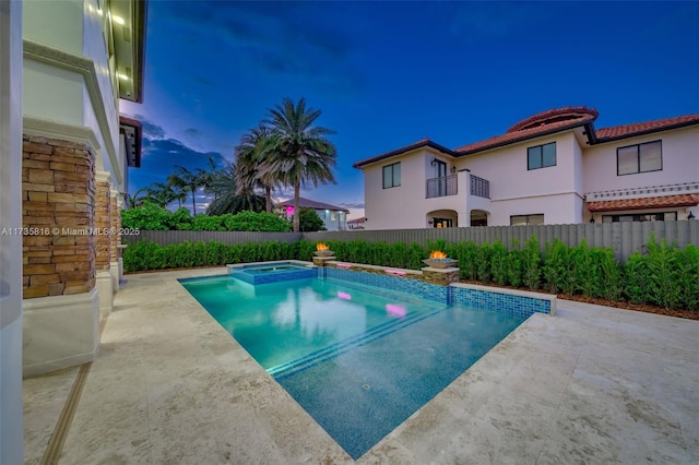 pool at dusk with an in ground hot tub and a patio