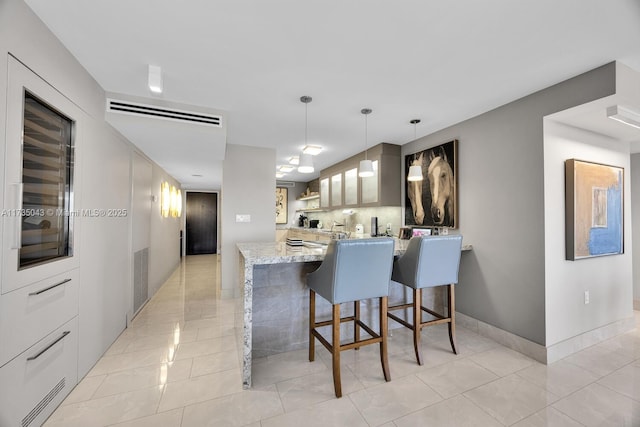 kitchen with a breakfast bar, decorative light fixtures, light tile patterned floors, kitchen peninsula, and light stone countertops