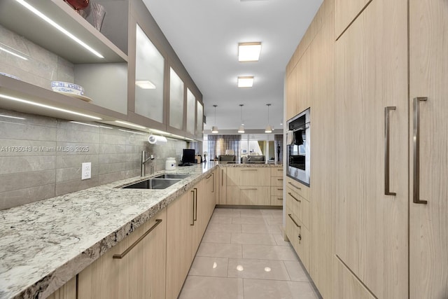 kitchen with light brown cabinetry, sink, backsplash, stainless steel oven, and light stone countertops