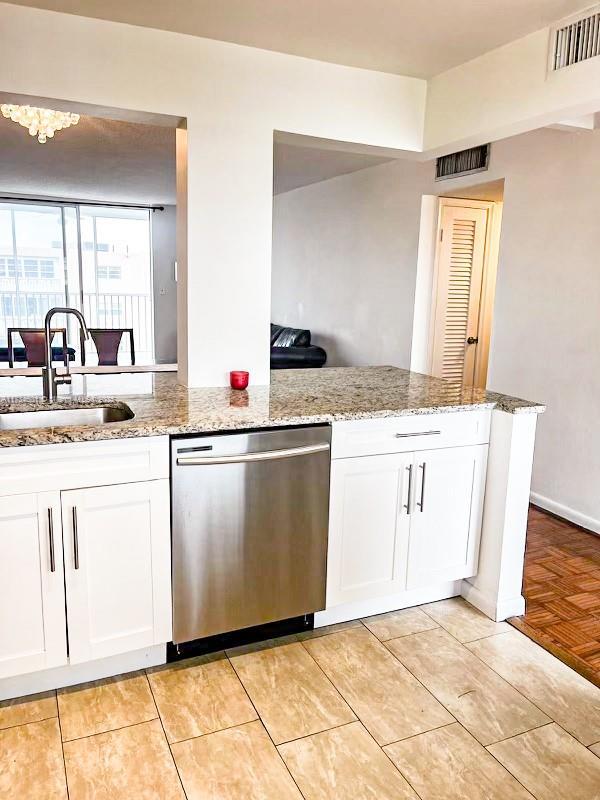 kitchen with white cabinetry, sink, stainless steel dishwasher, kitchen peninsula, and light stone countertops