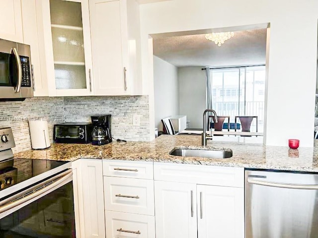 kitchen featuring stainless steel appliances, a sink, backsplash, white cabinetry, and glass insert cabinets