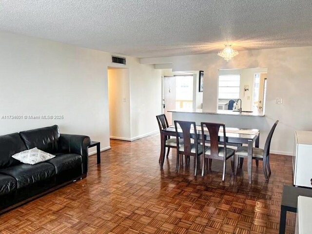 dining space with sink, a chandelier, a textured ceiling, and dark parquet floors