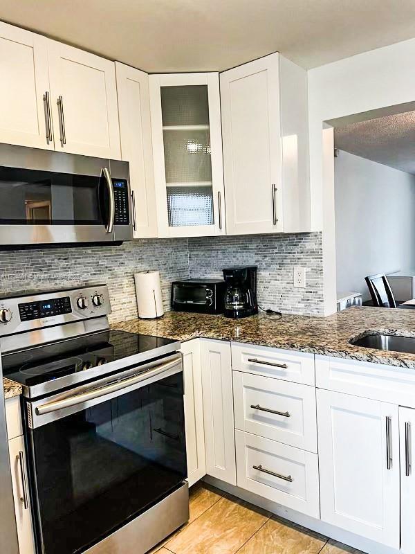 kitchen with white cabinets, decorative backsplash, dark stone counters, and appliances with stainless steel finishes
