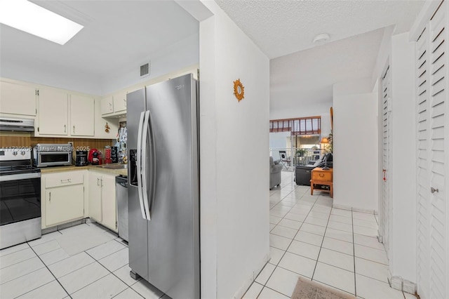 kitchen featuring extractor fan, appliances with stainless steel finishes, light tile patterned floors, cream cabinets, and a textured ceiling