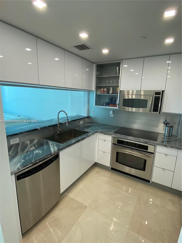 kitchen with dark stone countertops, stainless steel appliances, sink, and white cabinets