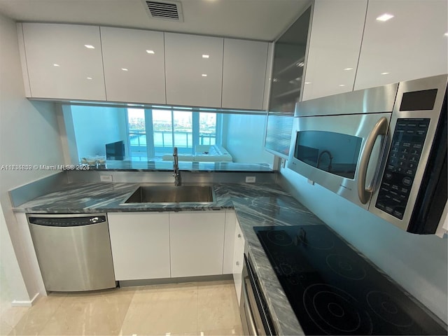 kitchen featuring stainless steel appliances, white cabinetry, sink, and dark stone countertops