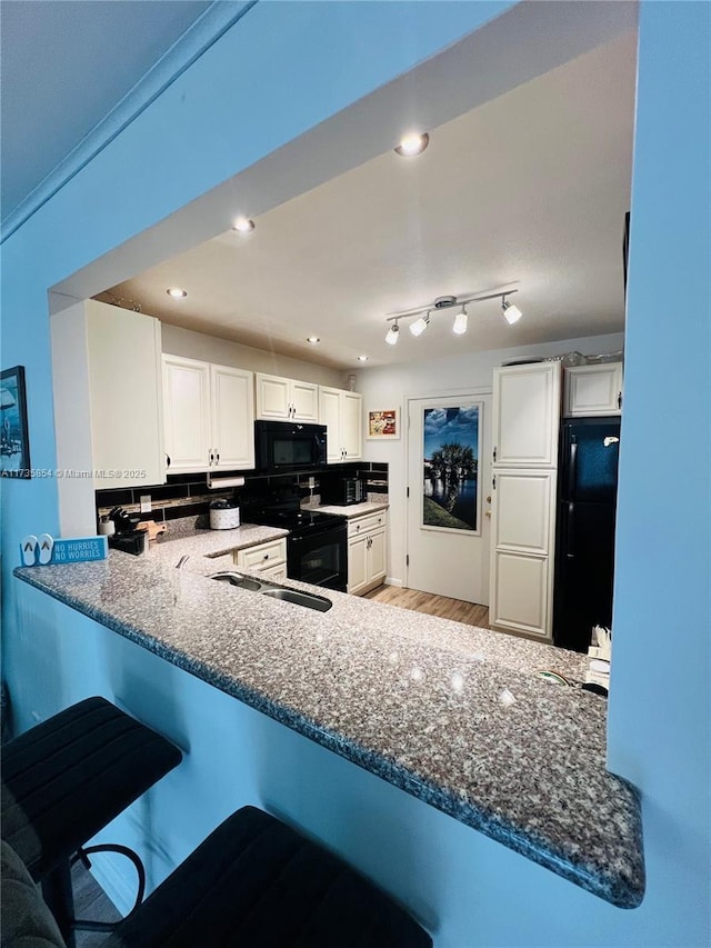 kitchen featuring white cabinetry, dark stone countertops, kitchen peninsula, and black appliances