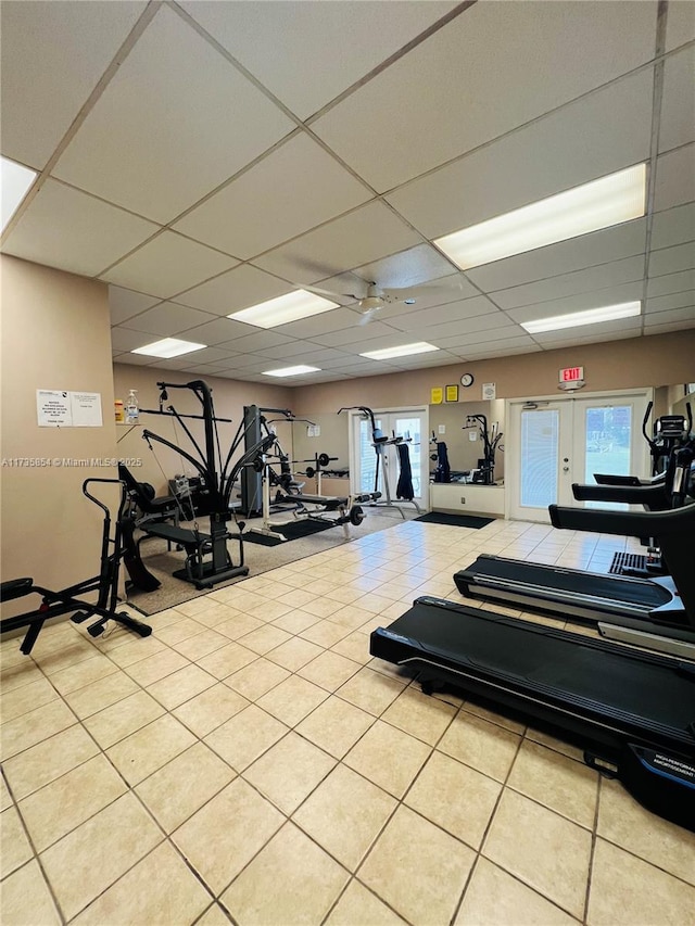 gym with light tile patterned floors, a paneled ceiling, and a healthy amount of sunlight