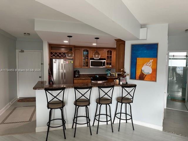 kitchen featuring pendant lighting, a kitchen bar, kitchen peninsula, stainless steel appliances, and light wood-type flooring