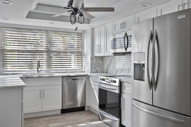 kitchen with appliances with stainless steel finishes, sink, white cabinets, decorative backsplash, and a tray ceiling