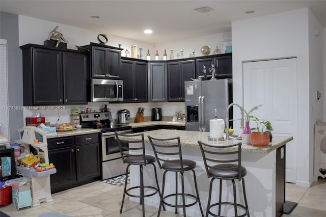 kitchen with an island with sink, appliances with stainless steel finishes, a breakfast bar, and light stone counters