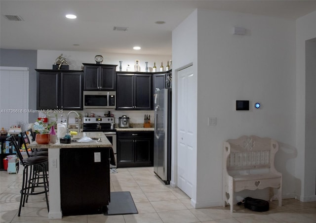 kitchen featuring light tile patterned flooring, appliances with stainless steel finishes, sink, a breakfast bar area, and light stone countertops