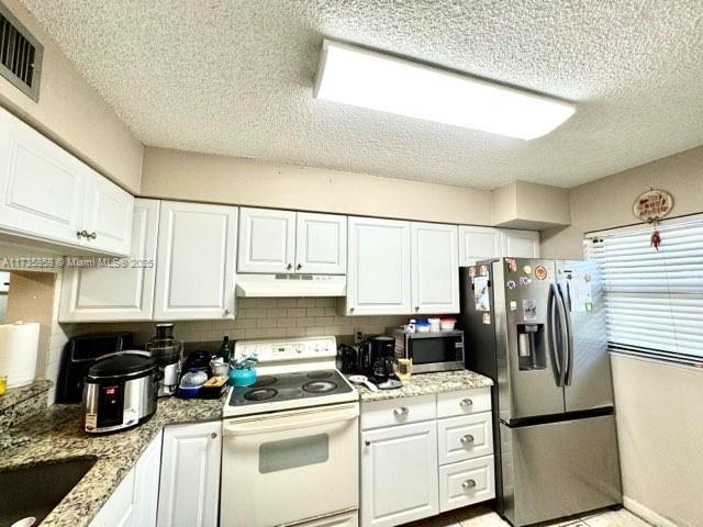 kitchen featuring appliances with stainless steel finishes, light stone counters, a textured ceiling, white cabinets, and decorative backsplash