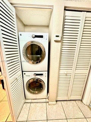 laundry area featuring stacked washer / dryer, light tile patterned floors, and a textured ceiling