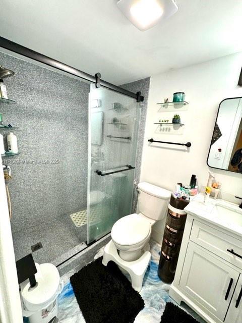 bathroom featuring vanity, a shower with shower door, and toilet