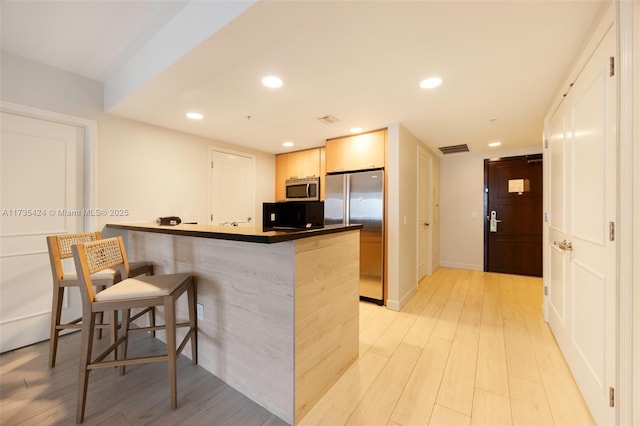 kitchen with a kitchen bar, light hardwood / wood-style floors, kitchen peninsula, and appliances with stainless steel finishes