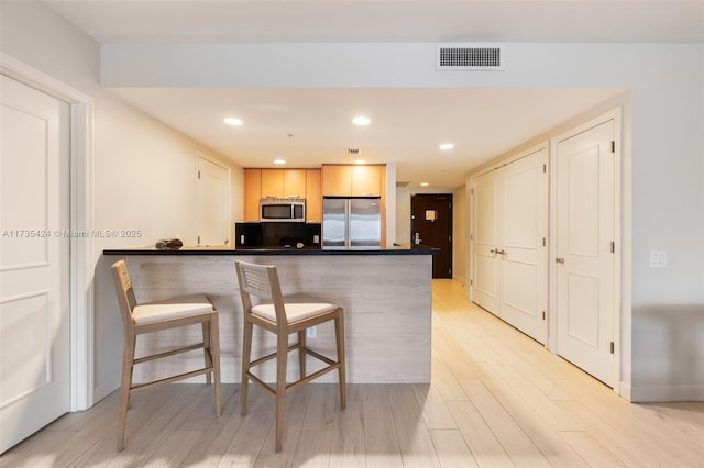 kitchen with appliances with stainless steel finishes, light brown cabinetry, kitchen peninsula, and light hardwood / wood-style floors