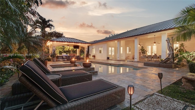 pool at dusk featuring a gazebo, outdoor lounge area, ceiling fan, and a patio area