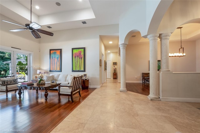 living room with ceiling fan, decorative columns, a high ceiling, light hardwood / wood-style floors, and a raised ceiling