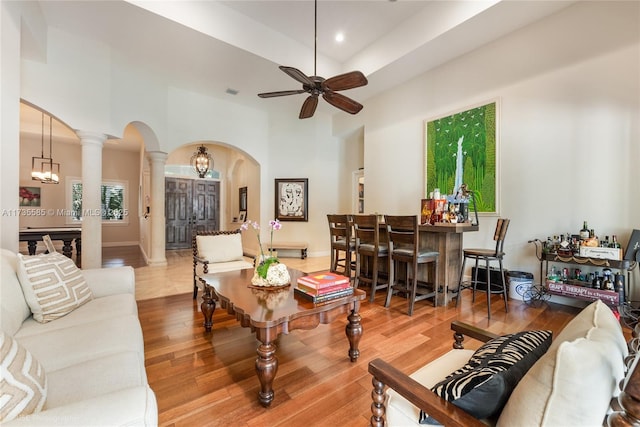 living room featuring hardwood / wood-style flooring, ceiling fan with notable chandelier, a high ceiling, and ornate columns