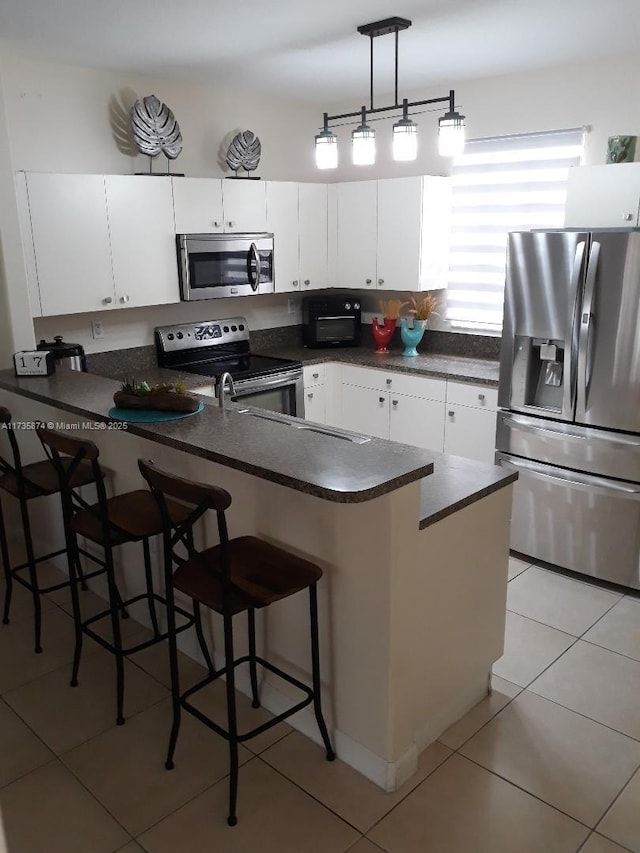 kitchen featuring stainless steel appliances, white cabinets, a kitchen bar, and kitchen peninsula