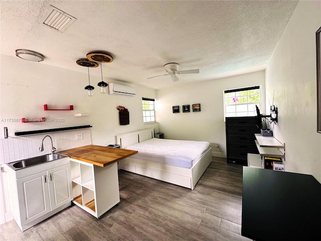 bedroom featuring dark hardwood / wood-style flooring, sink, multiple windows, and an AC wall unit