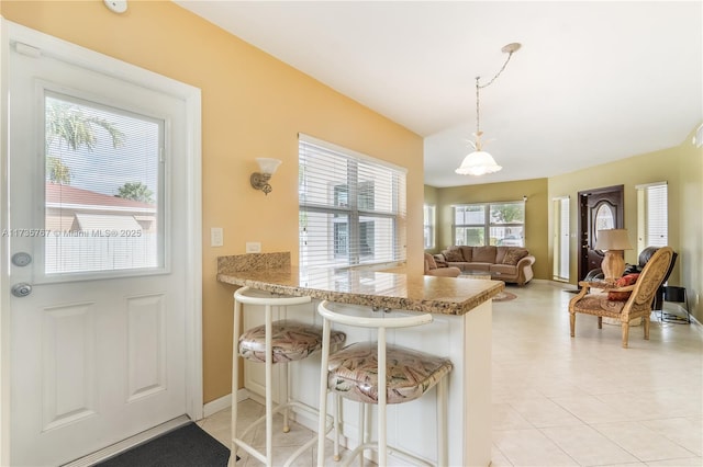 kitchen featuring pendant lighting, a breakfast bar area, light stone counters, vaulted ceiling, and kitchen peninsula