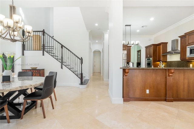 kitchen featuring wall chimney range hood, ornamental molding, stainless steel appliances, and hanging light fixtures