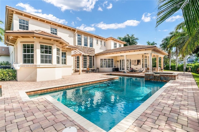 rear view of property with a swimming pool with hot tub and a patio