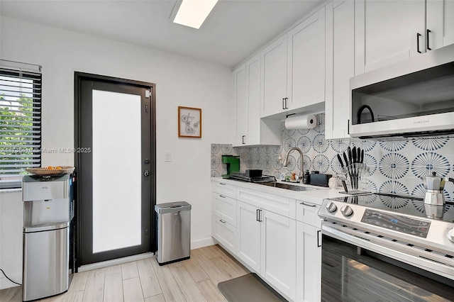 kitchen featuring sink, appliances with stainless steel finishes, white cabinetry, tasteful backsplash, and light wood-type flooring