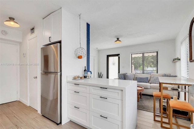 kitchen featuring stainless steel fridge, light wood-type flooring, and white cabinets