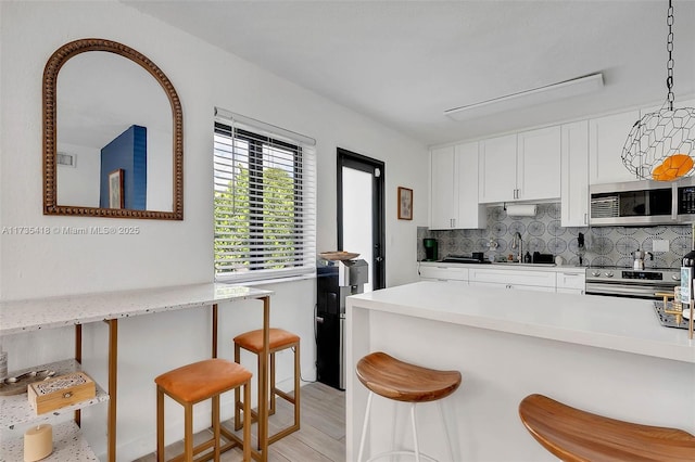 kitchen with white cabinetry, decorative light fixtures, appliances with stainless steel finishes, a kitchen breakfast bar, and backsplash