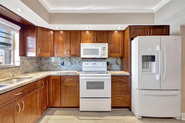 kitchen featuring white appliances, brown cabinets, crown molding, and light stone countertops