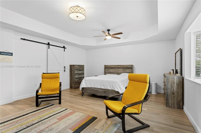 bedroom with ceiling fan, a barn door, a raised ceiling, and light hardwood / wood-style floors