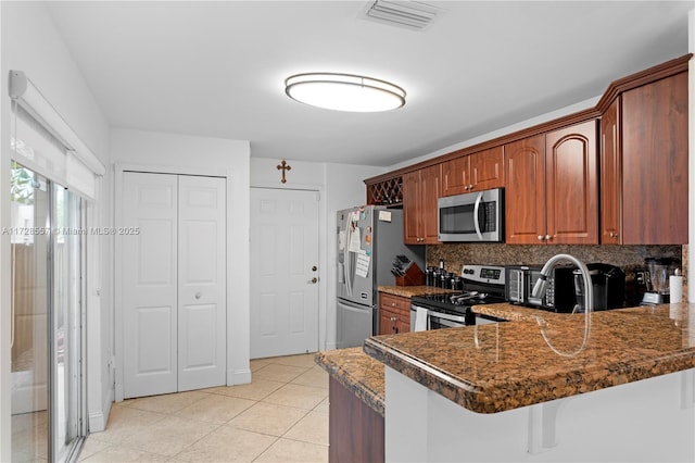 kitchen featuring light tile patterned floors, dark stone countertops, stainless steel appliances, tasteful backsplash, and kitchen peninsula