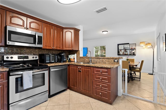 kitchen with stone countertops, sink, stainless steel appliances, light tile patterned flooring, and kitchen peninsula