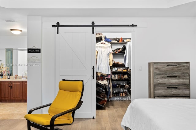 bedroom with ensuite bathroom, a walk in closet, a closet, a barn door, and light hardwood / wood-style floors