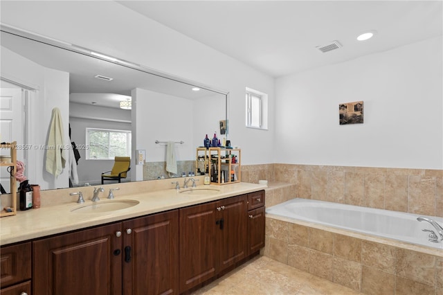 bathroom with vanity, a relaxing tiled tub, and plenty of natural light