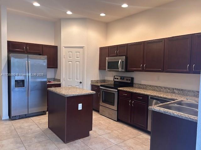 kitchen featuring sink, light tile patterned floors, appliances with stainless steel finishes, dark brown cabinets, and a kitchen island