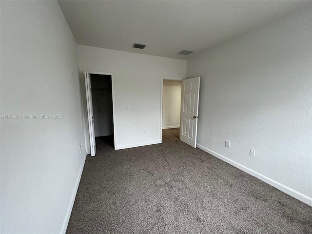 unfurnished bedroom featuring a walk in closet, a closet, and dark colored carpet