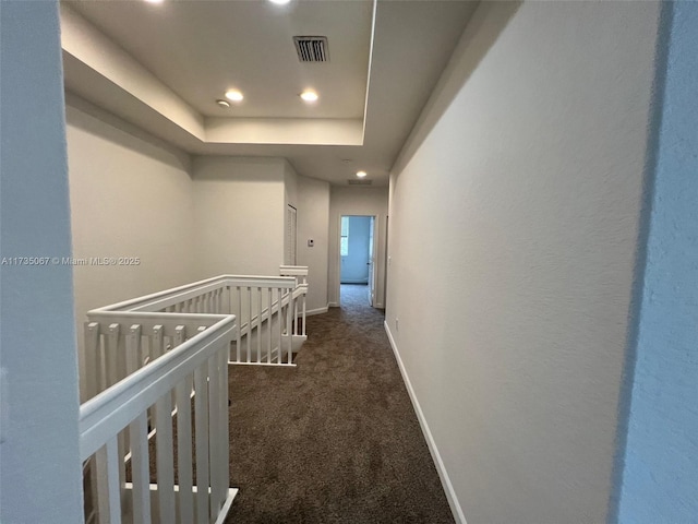 hall with a tray ceiling and dark carpet