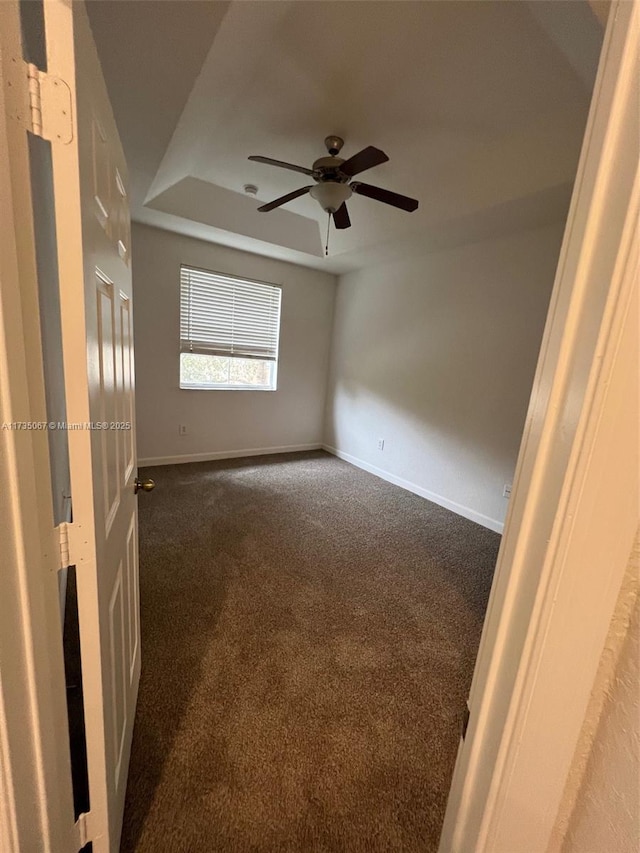 empty room featuring ceiling fan, a tray ceiling, and carpet floors