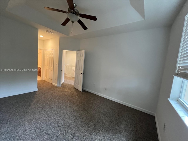 empty room with a tray ceiling, dark carpet, and ceiling fan