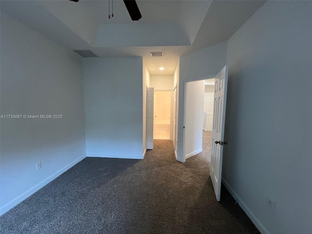 empty room with ceiling fan, a tray ceiling, and dark colored carpet