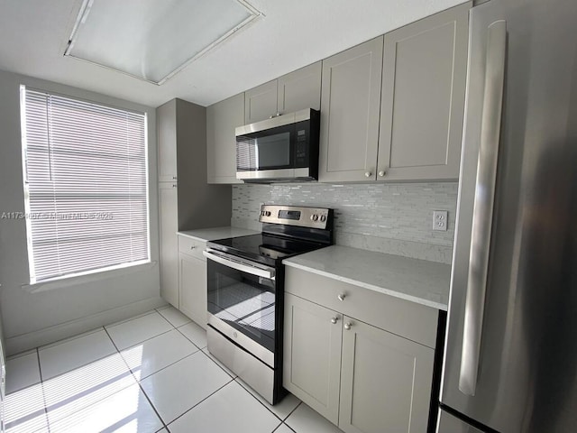 kitchen with backsplash, appliances with stainless steel finishes, light tile patterned floors, and gray cabinetry